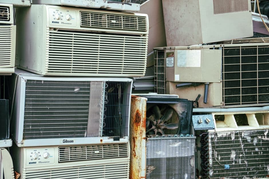 HVAC technician using a manifold gauge set to service an outdoor air conditioning unit, the same type of equipment used during R-22 refrigerant recovery and phaseout work