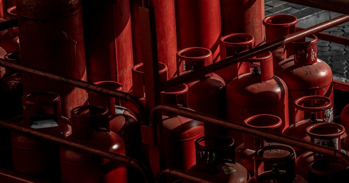 Rows of industrial red gas cylinders stored in a warehouse setting, representing the certified reclaimed refrigerant supply chain — recovered, reprocessed to AHRI-700 purity, and tracked through chain-of-custody documentation under 40 CFR Part 84 Subpart C