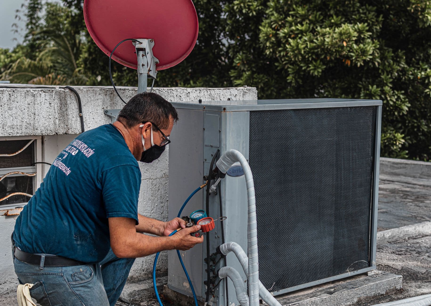 An HVAC technician using a manifold gauge to service an outdoor air conditioning unit, illustrating the certified Section 608 work that equipment owners must verify under EPA refrigerant rules.
