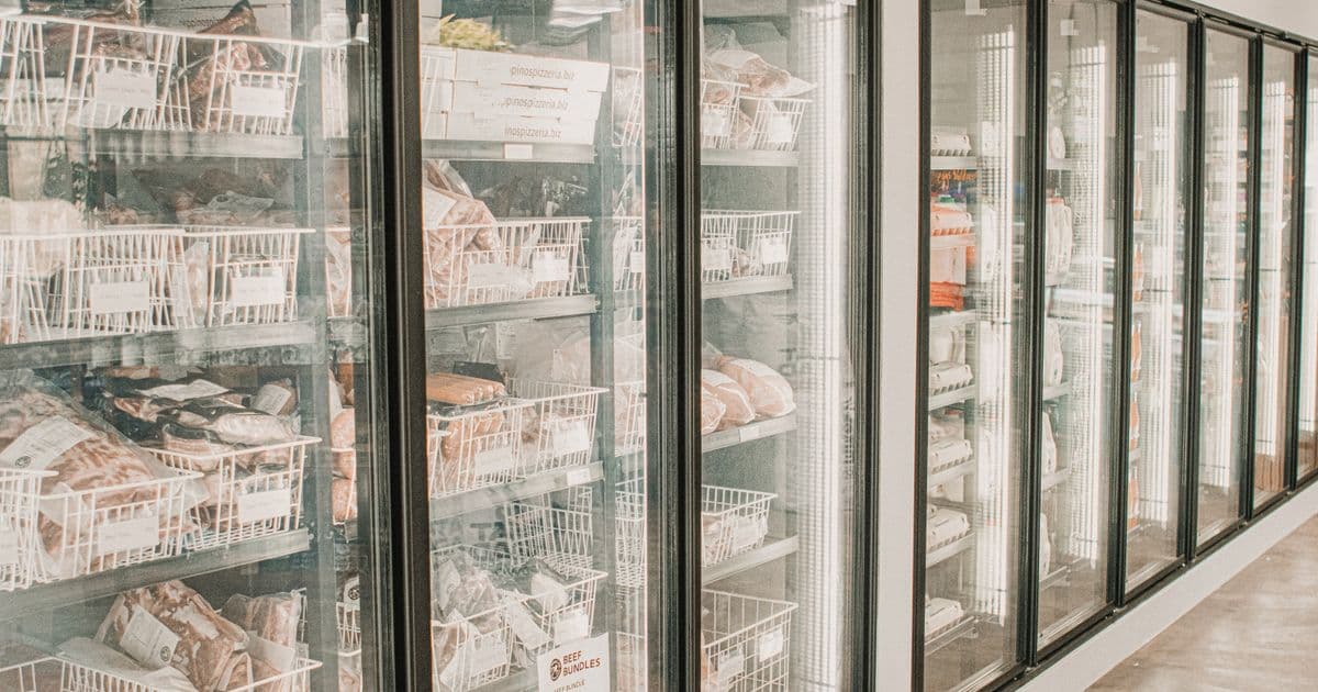 Long aisle of glass-door supermarket freezer cases with frozen products visible behind transparent doors, representing the large distributed refrigeration systems regulated under 40 CFR Part 84 Subpart C